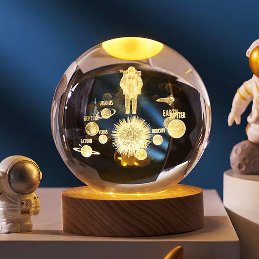 Decorative glass sphere with engraved solar system design on a wooden base, surrounded by astronaut figurines.
