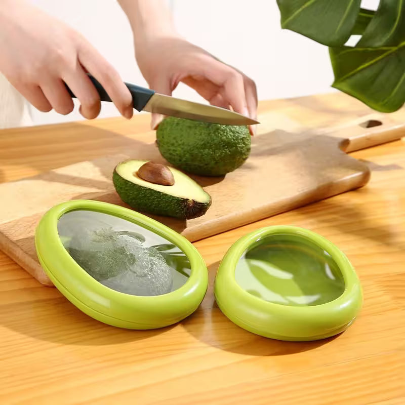 Person cutting an avocado on a wooden board with a knife, next to two green avocado holders.