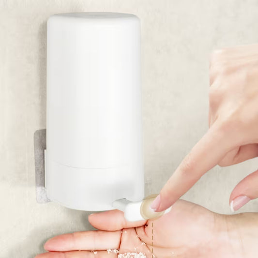 Hand using a wall-mounted soap dispenser on a beige background