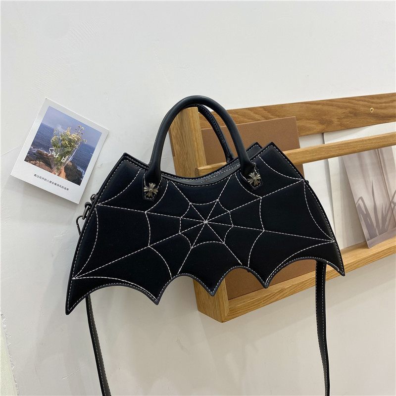 Black bat-shaped handbag with spider web design on a white surface.