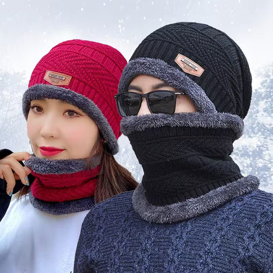 Two people wearing matching knitted hats and scarves with a snowy background.