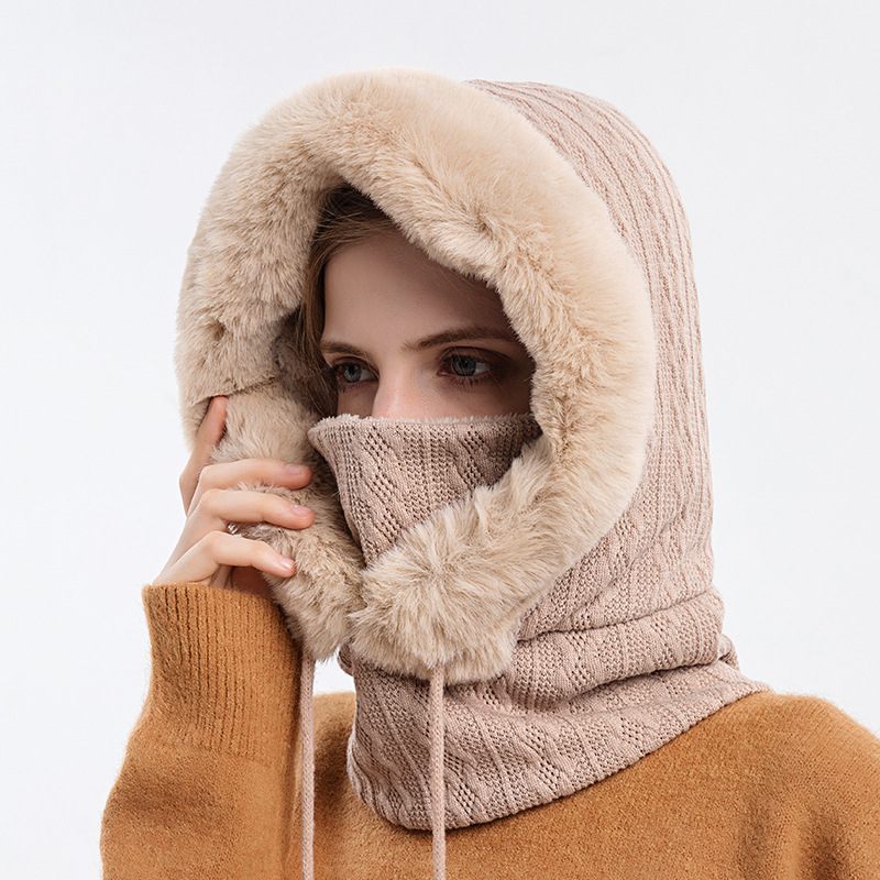 Person wearing a beige knitted balaclava with fur trim on a white background