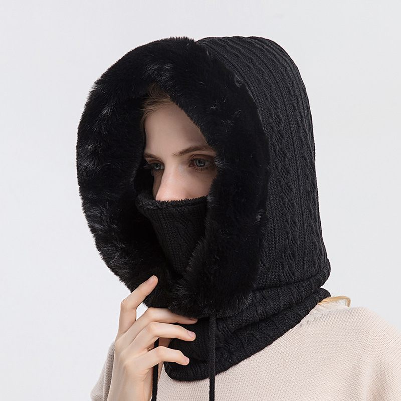 Person wearing a black knitted hood over their head and face on a light gray background