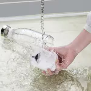 Hand washing a dish under running water with soap bubbles.