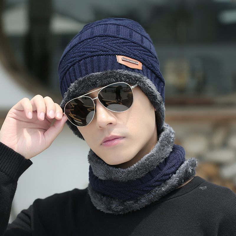 Person wearing a navy blue knitted hat and gray scarf with sunglasses, blurred background