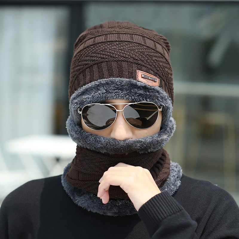 Person wearing a brown knitted hat and gray scarf with sunglasses on a blurred background