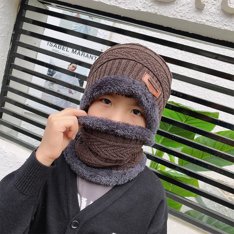 Child wearing a brown and gray winter hat and scarf against a striped background