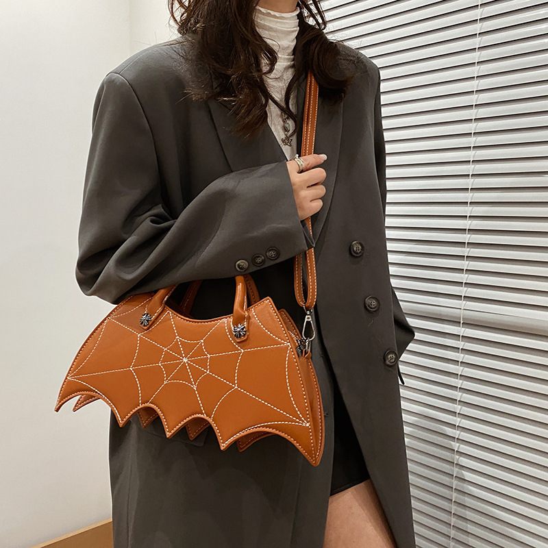 Person holding a brown bat-shaped handbag with spider web design.