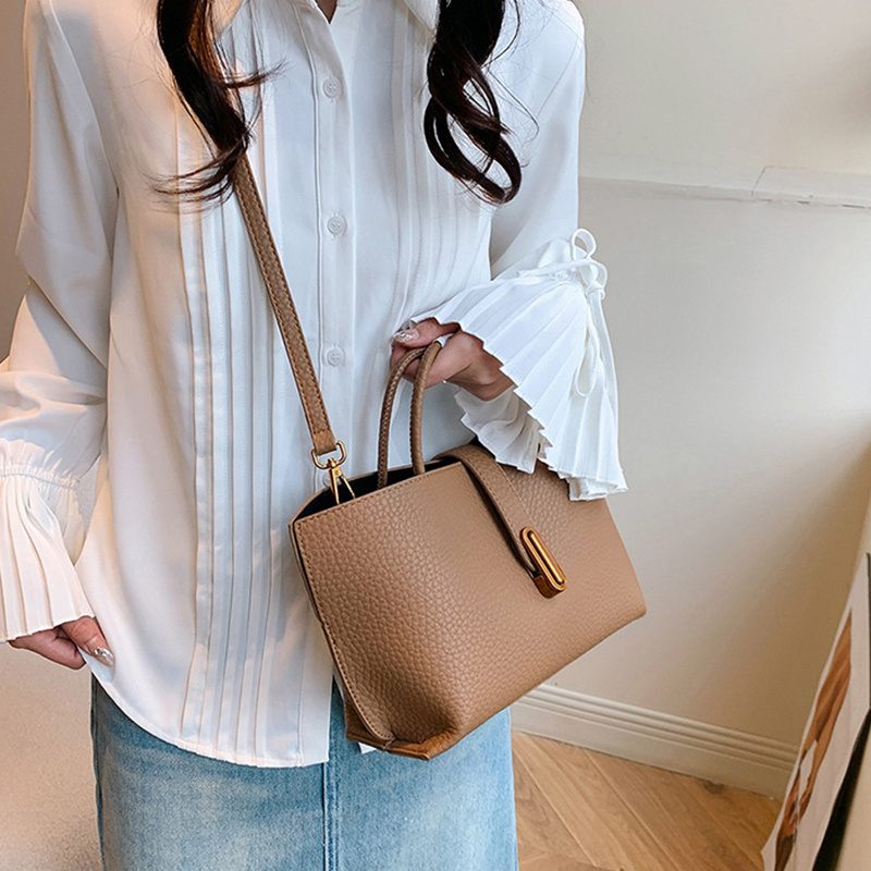 Person holding a beige handbag wearing a white blouse and blue jeans indoors.