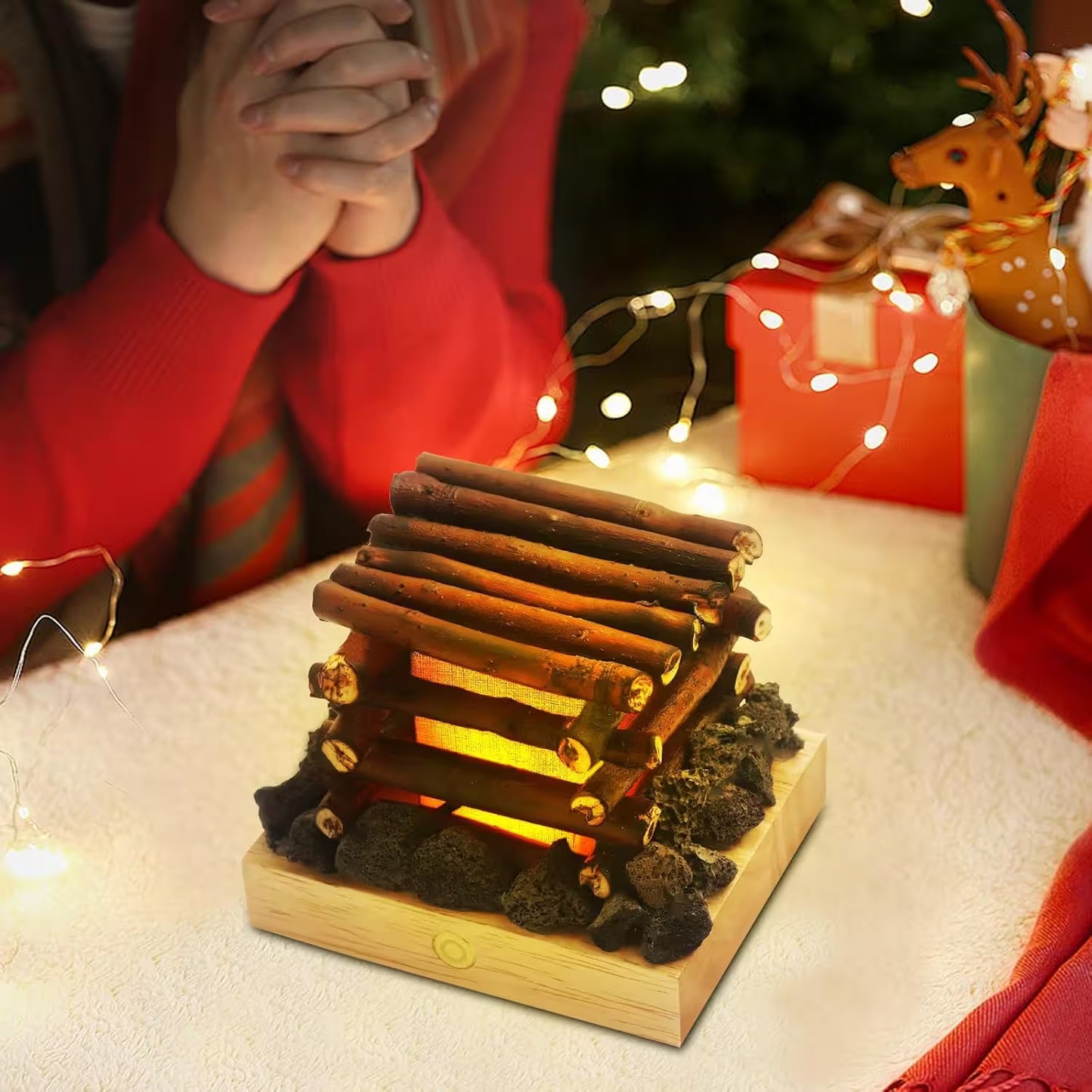 Decorative log cabin with glowing interior on a table with Christmas decorations.