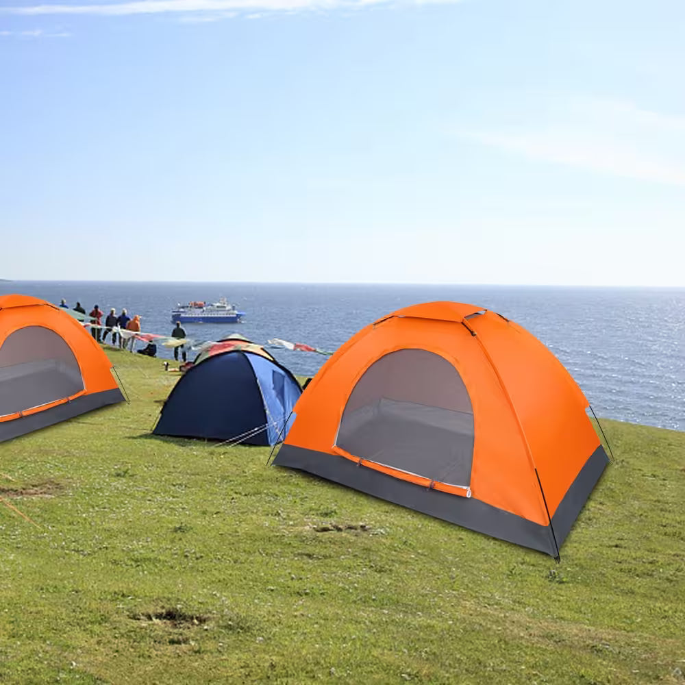 Orange and blue tents set up on a grassy area near a body of water with people in the background.