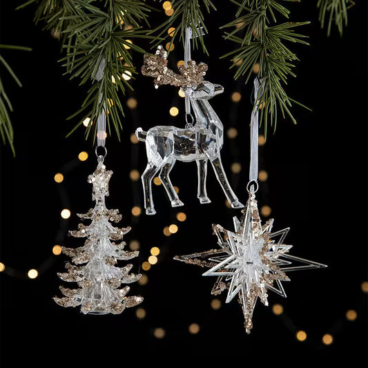 Crystal reindeer, tree, and star ornaments hanging on a Christmas tree with blurred lights in the background.