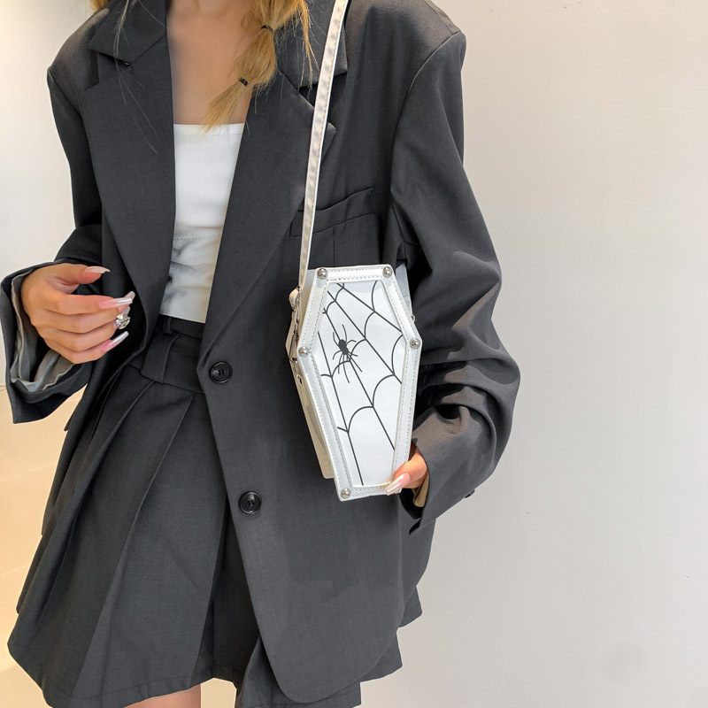 Person wearing a black blazer holding a unique handbag with spider web design.
