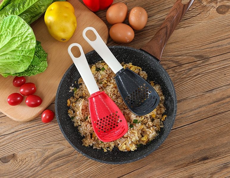 Fried rice in a pan with two silicone spatulas, surrounded by vegetables on a wooden surface.