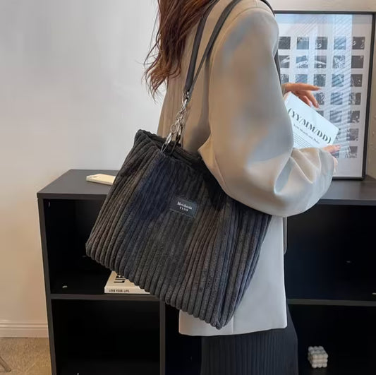 Person holding a textured gray bag with a visible brand logo in an indoor setting.