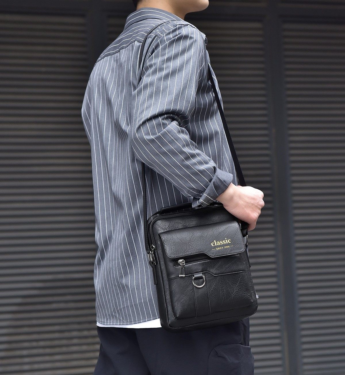 Person holding a black leather bag with 'classic' branding against a metallic background