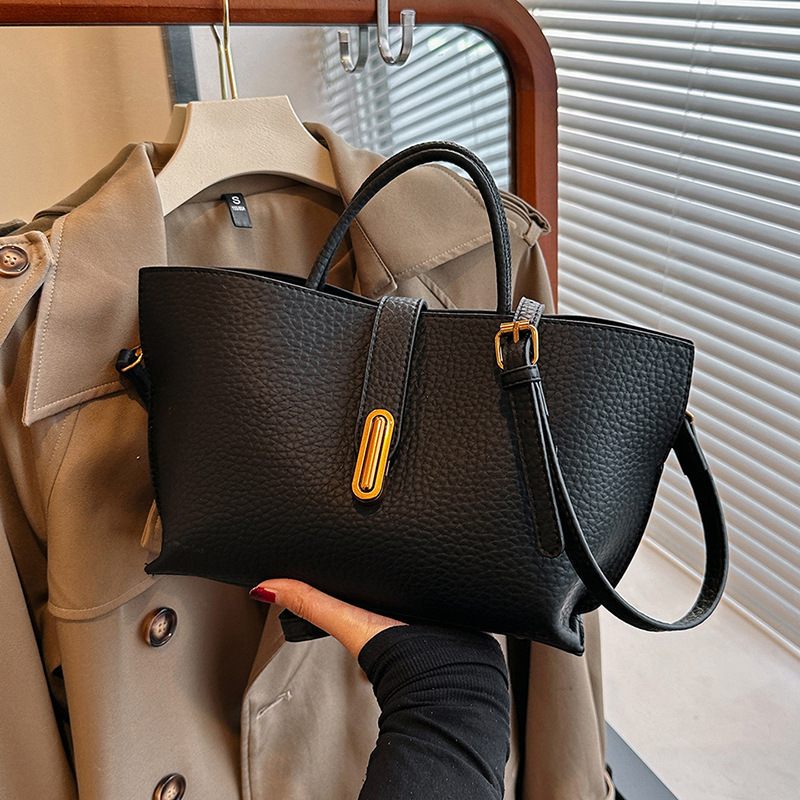 Black handbag held in front of a beige trench coat on a hanger.