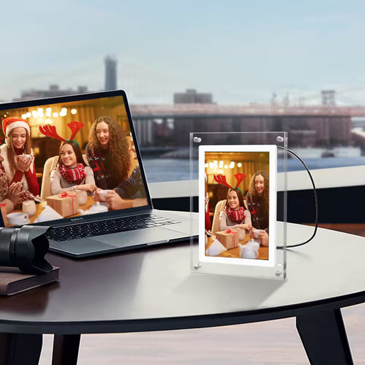 Laptop displaying a video call with people in festive attire, next to a transparent photo frame on a table.