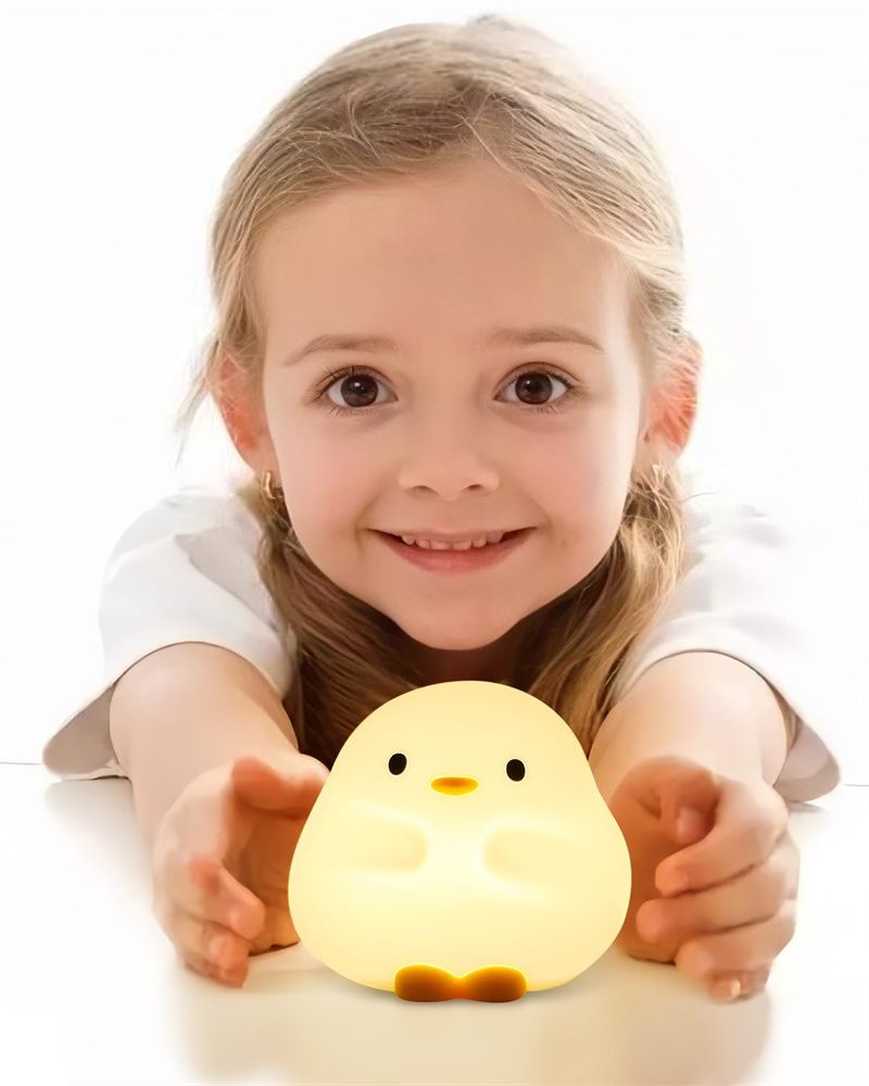 Child holding a small, round, yellow night light shaped like a chick on a white background