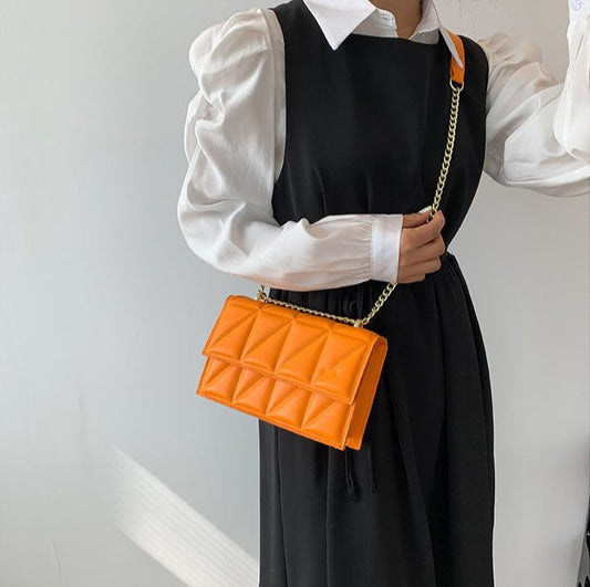 Person holding an orange quilted handbag with a white shirt and black dress against a light gray background