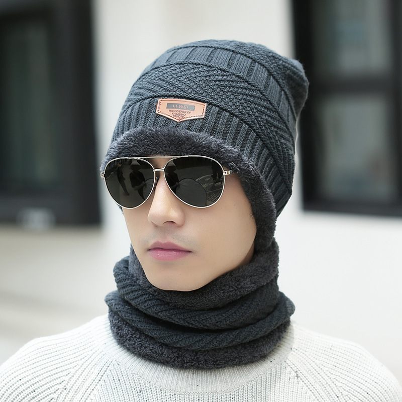 Person wearing a dark gray knit beanie and scarf set with sunglasses on a blurred background