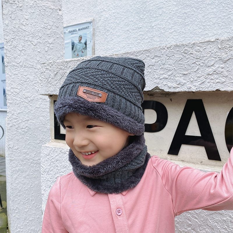 Child wearing a gray knit hat and scarf in front of a white wall with text.