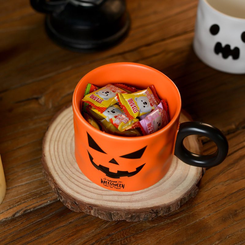 Halloween-themed orange mug with black handle filled with candy on a wooden surface.