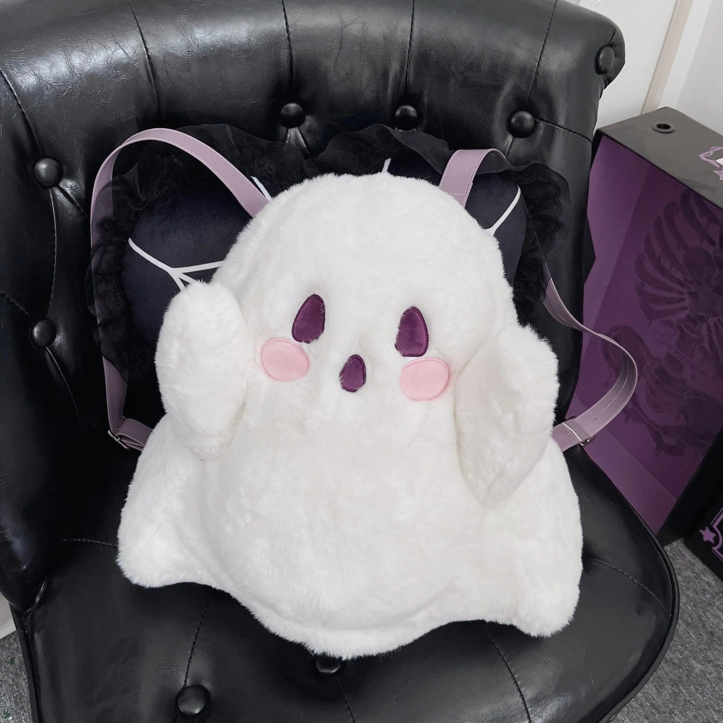 White plush ghost backpack with purple eyes and pink cheeks on a black chair.