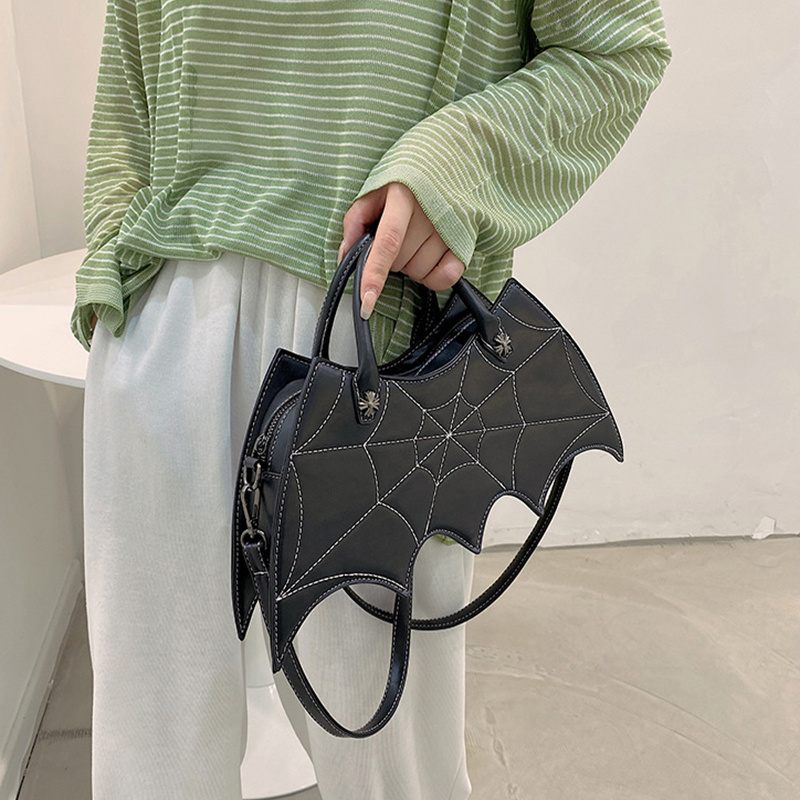 Person holding a black bat-shaped handbag with a spider web design.