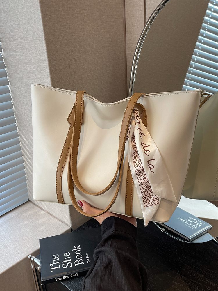 Beige handbag with brown handle and strap, accompanied by a small black book and a blue card on a textured surface.