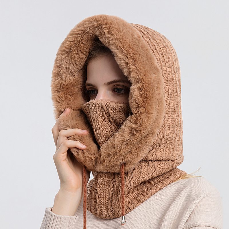 Person wearing a brown knitted hood with fur trim on a light gray background