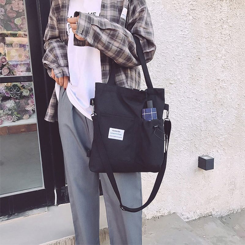 Person holding a black tote bag against a light-colored wall.
