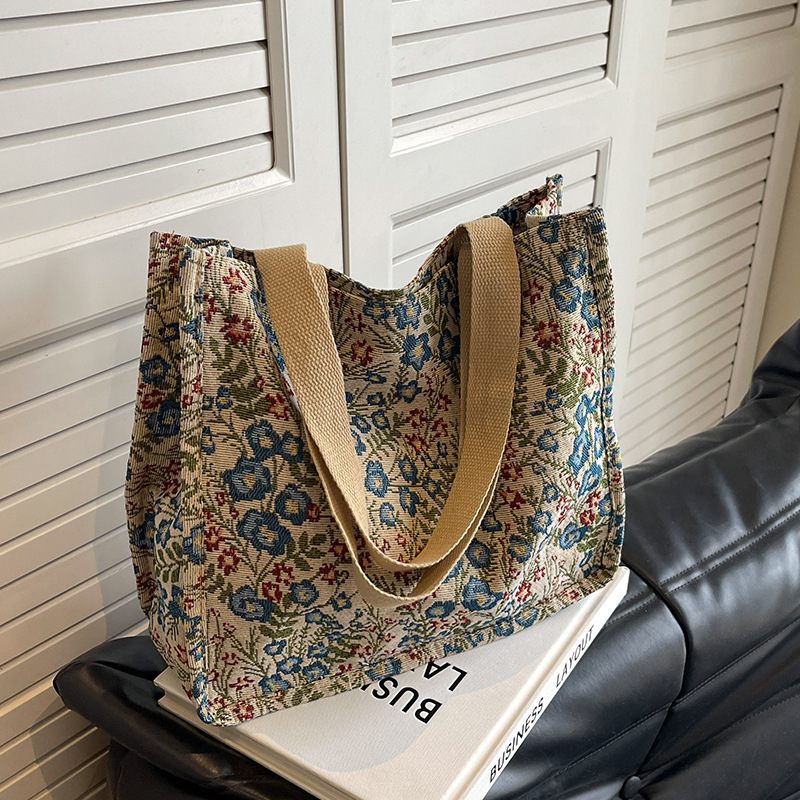 Floral patterned tote bag with beige handles on a black surface against a white shutter background