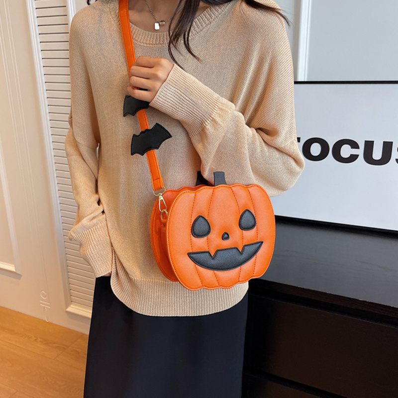 Person wearing a beige sweater holding an orange pumpkin-shaped bag with black bat designs.