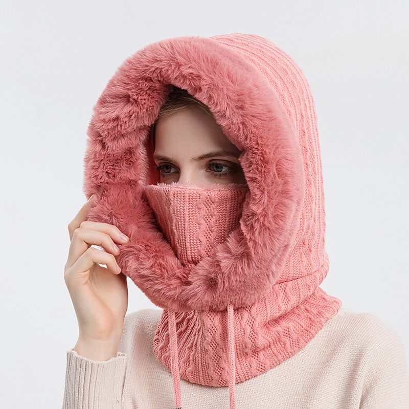 Person wearing a pink knitted hood with fur trim on a light gray background