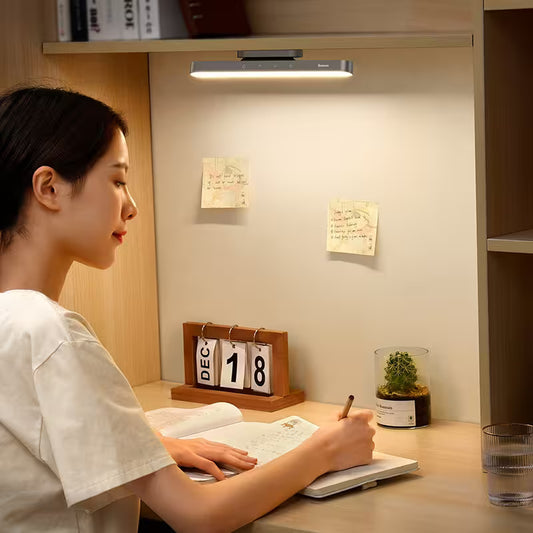 Person studying at a desk with a light fixture above, near a calendar and plant.