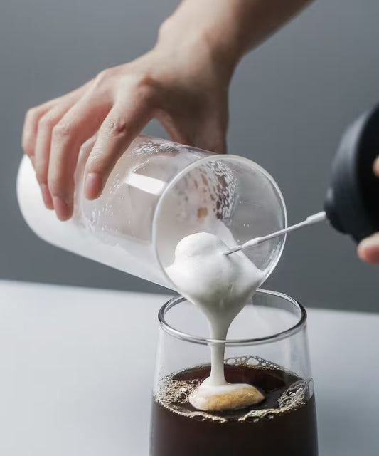 Pouring whipped cream into a glass of coffee with a gray background