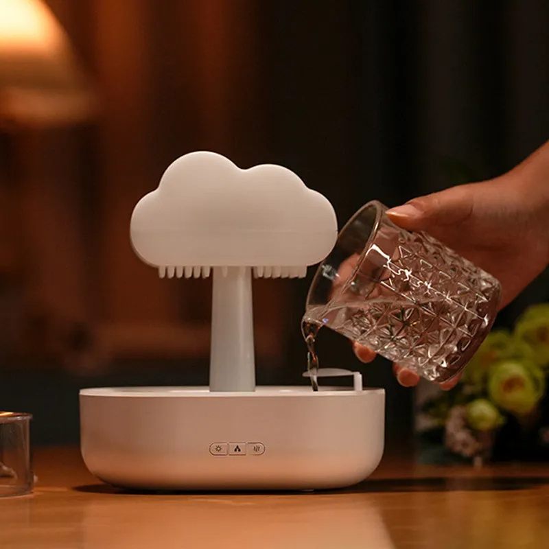 Cloud-shaped humidifier on a table with a hand pouring water into it.