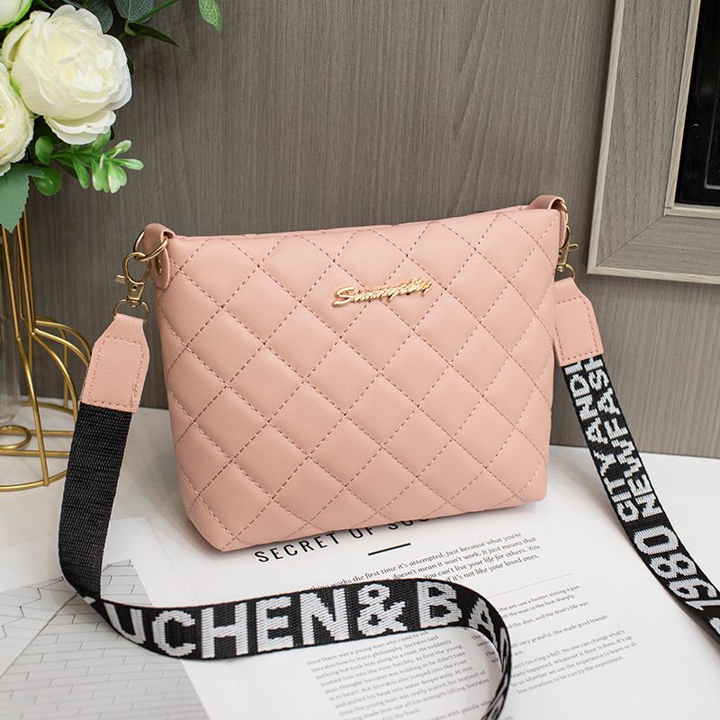 Pink quilted handbag with a black strap on a surface with flowers and text in the background