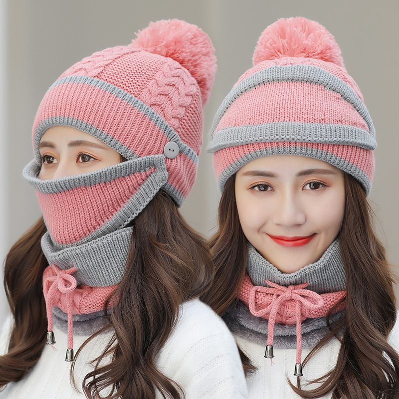 Two pink and gray knitted hats with face masks worn by a model on a plain background