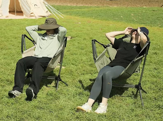 Two people relaxing on camping chairs in a grassy field.