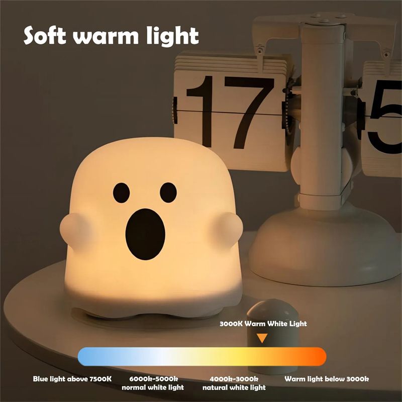 Ghost-shaped night light emitting a soft warm light, with a calendar and lamp in the background.