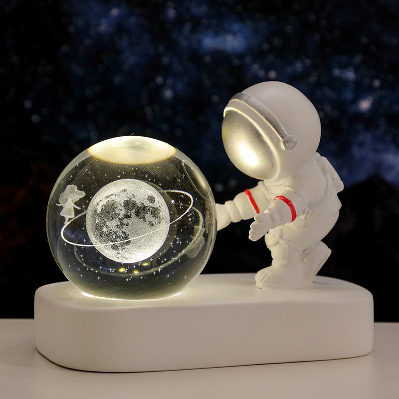 Spaceman figurine interacting with a glowing sphere displaying a celestial scene on a dark background