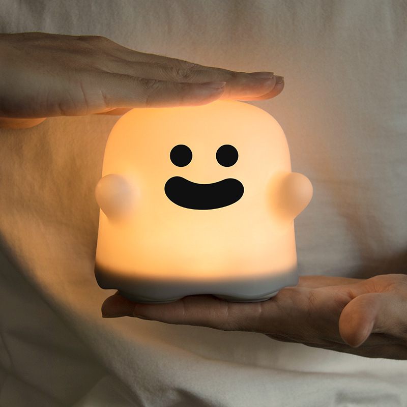 Person holding a glowing ghost-shaped night light with a smiling face.