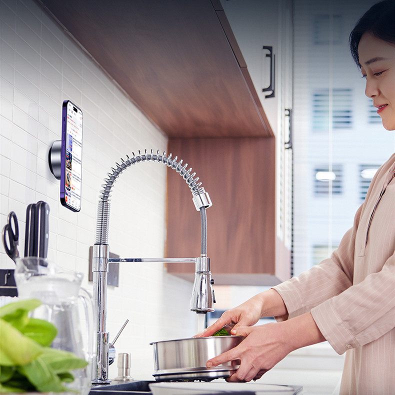 Person washing dishes in a kitchen with a modern faucet and smartphone displaying an app.