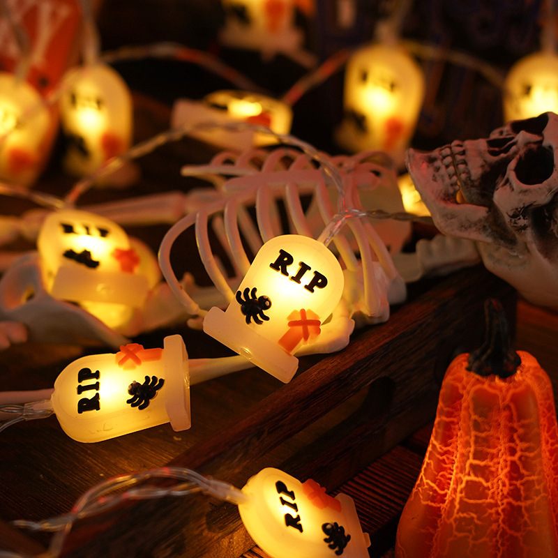 Halloween-themed string lights with ghost and tombstone designs on a dark background.