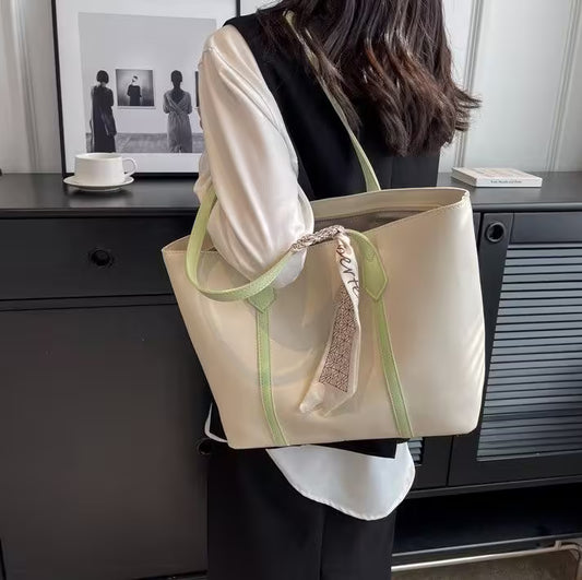 Person holding a beige tote bag with green straps in an indoor setting.