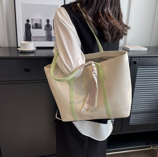 Person holding a beige tote bag with green straps in an indoor setting.
