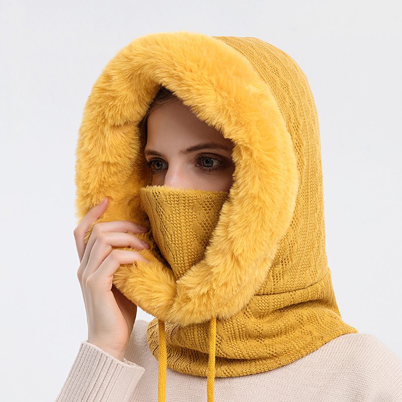 Person wearing a mustard yellow knitted hood with fur trim on a light gray background