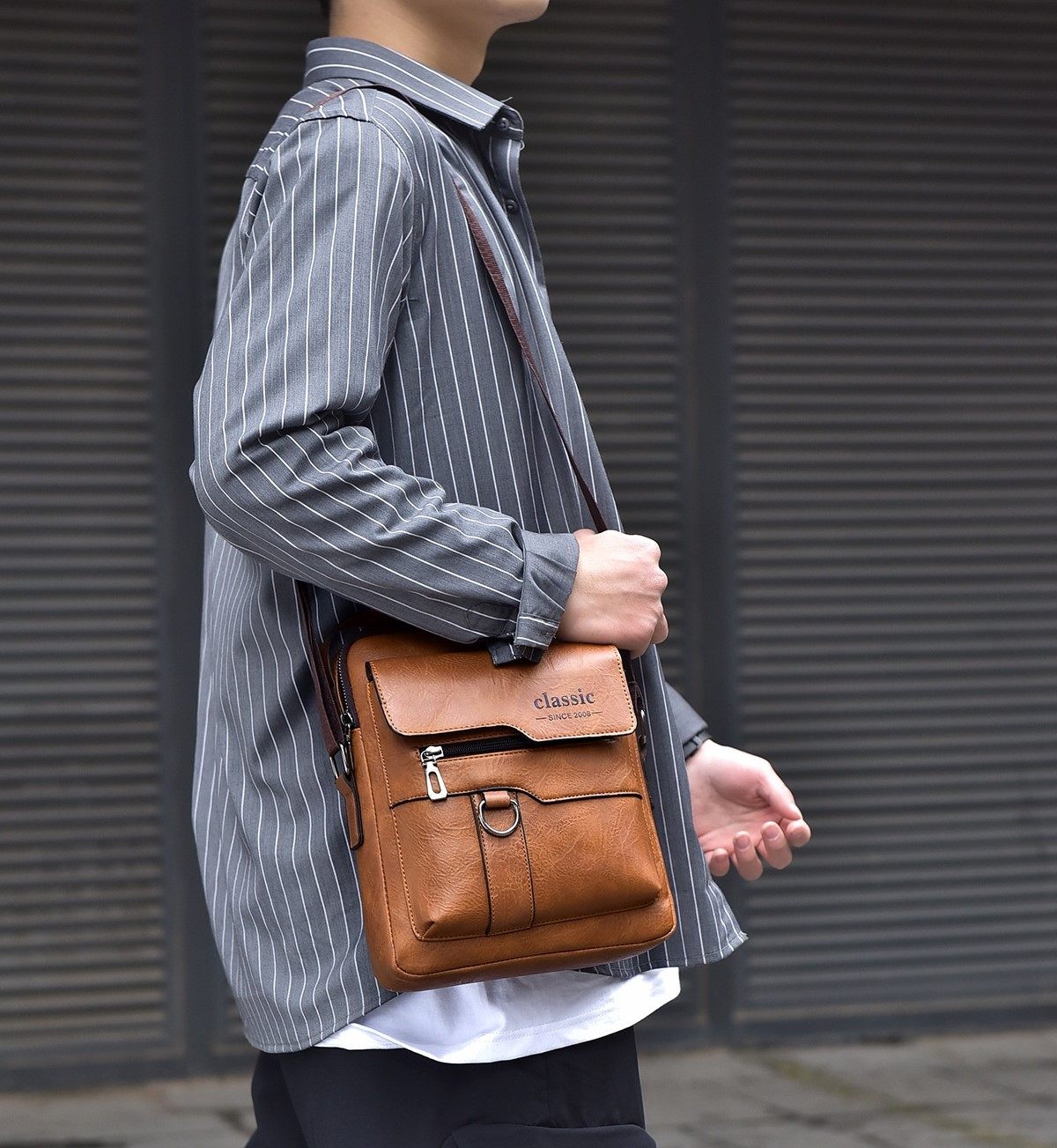Person holding a brown leather bag with 'classic' branding against a gray background